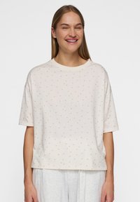 Kortærmet t-shirt i cremefarvet, lavet af blødt stof med en rund halsudskæring og et mønster af små guldprikker.