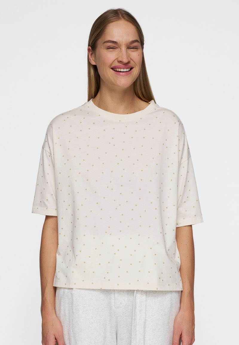Kortærmet t-shirt i cremefarvet, lavet af blødt stof med en rund halsudskæring og et mønster af små guldprikker.