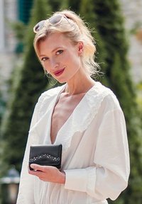 Black leather wallet with a curved design featuring silver and colored embellishments, held by a person in a white blouse with lace accents.