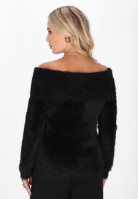 Maglione nero, a spalle scoperte, con una texture morbida e pelosa. Maniche lunghe e un design aderente, presenta un ampio scollo.