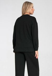 Czarna, oversize bluza z długim rękawem, z prążkowanymi mankietami i prostym dołem. Wykonana z miękkiego materiału, ozdobiona subtelnym szwem z tyłu.