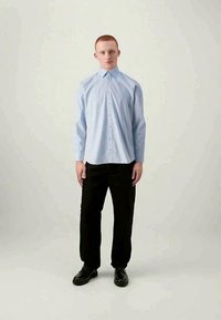 Cămașă albă-albăstrie cu mâneci lungi și guler ascuțit, combinată cu pantaloni negri și pantofi negri, prezentată pe un fundal neutru.