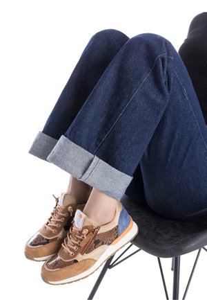 Zapatillas deportivas en beige, marrón y azul con texturas mixtas, paneles estampados y cordones claros. Combinadas con unos vaqueros oscuros arremangados.