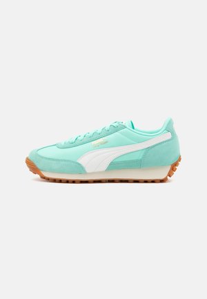 Basket en daim vert menthe avec des accents blancs, dotée d'une semelle en caoutchouc, d'un laçage et d'un logo doré. Forme classique de chaussure de course.