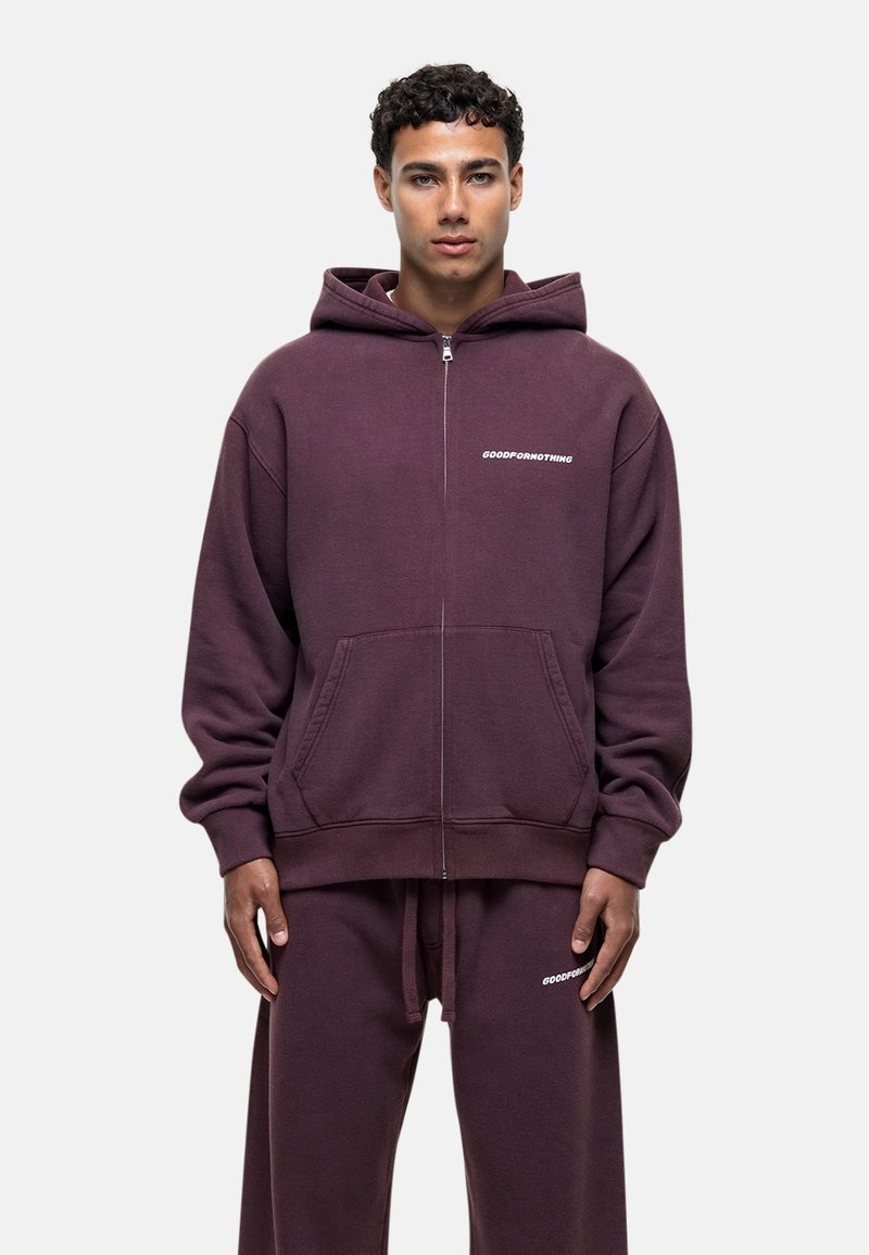 Sweat à capuche zippé bordeaux en tissu peluche, avec poches avant et un logo "GOODFORNOTHING" blanc sur la poitrine. Coupe décontractée et confortable.