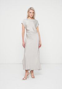 Robe longue, gris clair, en tissu lisse et fluide avec des manches courtes et une coupe décontractée, associée à des sandales à talons beiges.