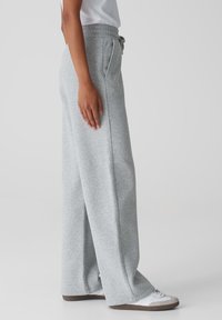 Grijze wijde sweatpants gemaakt van een zachte katoenmix, met een elastische tailleband, een trekkoord en zijzakken. Gepaard met witte sneakers.
