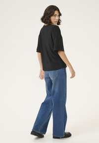 Haut plissé noir à coupe ample et manches courtes, assorti à un jean en denim bleu taille haute et des chaussures noires à semelles épaisses.
