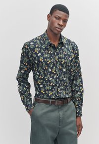 Langærmet skjorte med blomsterprint i mørkeblå, prydet med appelsiner og hvide blomster. Blødt stof, knappet krave, kombineret med grønne bukser.