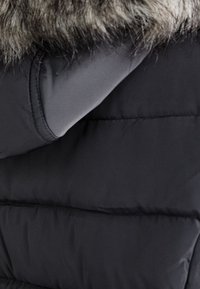 Zwarte pufferjack met een gladde stof en een gequiltde textuur. De kraag heeft een grijze nepbontafwerking voor extra detail.