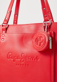 Borsa tote in pelle rossa con logo "Pepe Jeans London" in rilievo. Include un borsellino rotondo staccabile con superficie testurizzata e zip.