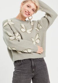 Pull en maille gris clair avec des motifs de papillons texturés blancs et verts, doté d'un col ras du cou et d'un design légèrement court.