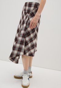 Falda de cuadro con dobladillo asimétrico, predominantemente en tonos rojos y grises, y de tela suave; llevada con zapatillas blancas y calcetines grises.