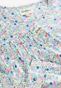 Ziedu blūze ar zilu fonu, kurā redzami rozā un baltie ziedi. Kokvilnas audums, savāktie detaļas apkaklē un redzamas zīmolu etiķetes.
