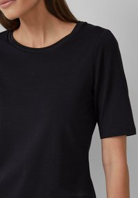 T-shirt noir à manches courtes en tissu doux et lisse, avec un col rond et des coutures propres et simples.