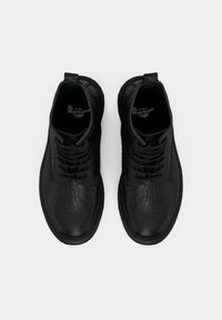 Par crnih Dr. Martens čizama s teksturom kože s uzorkom krokodila, crnim vezicama i debelim gumenim đonovima, prikazanim odozgo na bijeloj pozadini.