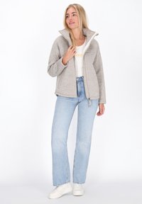 Lichtgrijze fleece jas met een hoge kraag en ritssluiting aan de voorkant. Gecombineerd met lichtblauwe recht gesneden jeans en witte sneakers.