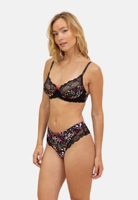 Bralette en dentelle et culotte assortie en noir avec une broderie florale multicolore. Comprend des bords festonnés et des nœuds sur le soutien-gorge. Texture lisse.