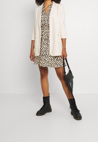 Beige blazer over a black and beige leopard print dress. Black lace-up combat boots and a small black bag with fringe details.
