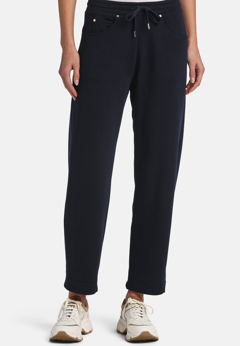 Woman wearing navy blue relaxed-fit drawstring pants and white lace-up sneakers, standing against a plain background.