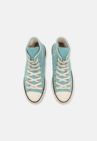 High-top sneakers in light blue canvas with cream laces and gold eyelets. Black rubber soles with white toe caps and stitching details.