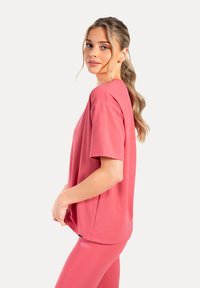 T-shirt rosa a maniche corte in tessuto morbido, con vestibilità comoda e dettaglio di marchio discreto vicino all'orlo. Abbinata a leggings coordinati.