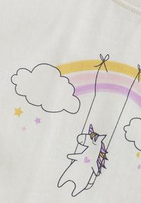 Vitt tyg med en lekfull enhörning som svänger, omgiven av moln och en regnbåge i gula och lila nyanser.