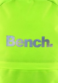 Neon zöld szövet hátizsák, amelyen jól látható ezüst "Bench." logó található. Sima tapintású, varrt részletekkel és egy biztonságos zsebbel.