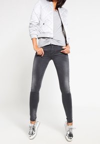 Gestepptes silbernes Bomberjackett, graues, tailliertes T-Shirt, dunkelgraue Skinny-Jeans und metallic-silberne Sneakers mit Quastenakzenten.