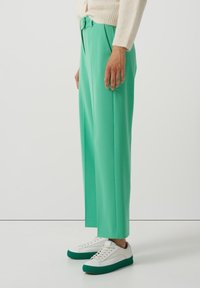 Gröna vida byxor i slätt tyg, med hög midja och bältedetalj. Matchas med vita och gröna sneakers.