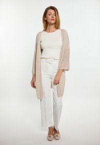 Lätt, beige kofta, öppen design med 3/4-ärmar, bärs över en vit ribbad topp och vita vida byxor, kombinerat med beige skor.