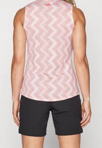 Červená a bílá vzorovaná bezramínková košile s zakřiveným lemem, spárovaná s černými šortkami. Tkanina vypadá lehce a hladce.