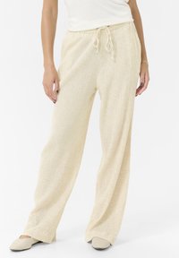 Pantalon large texturé de couleur crème, avec une taille élastique et un cordon de serrage. Fini lisse avec de légères rayures verticales.