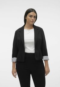 Sort blazer med opvaskede stribede ærmer, parret med en hvid top. Modellen bærer sorte bukser. Enkel, skræddersyet design.