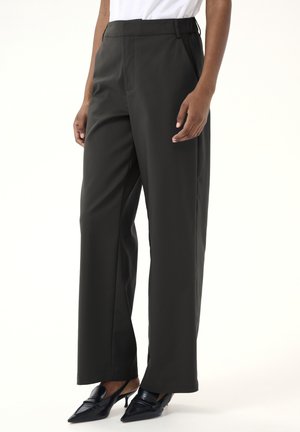 Dark green wide-leg trousers with a smooth texture, high waist, and side pockets; paired with pointed black heels for contrast.