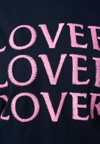 Marine t-shirt met grote, geborduurde roze letters die het woord "LOVE" in herhaalde patronen spellen. Glad stoffen textuur met ronde stiksels.