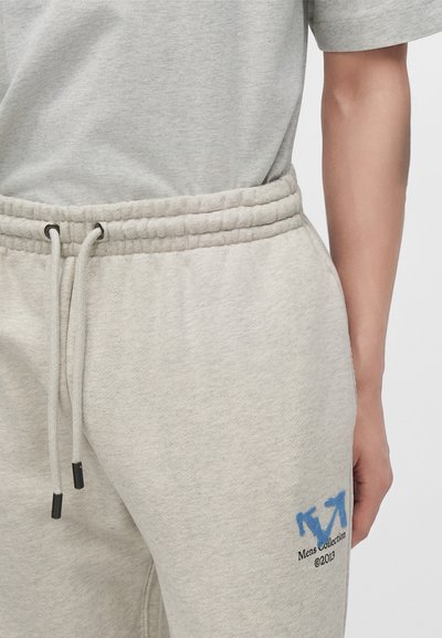 Pantalon de survêtement gris clair avec taille élastique et cordon, comportant des flèches bleues et un petit texte noir ""Mens Collection ©2013"" sur la partie supérieure de la cuisse.