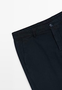 Pantalon bleu marine foncé montrant la section supérieure avec fermeture à bouton, passants pour ceinture et bordures supérieures des poches latérales sur fond blanc.