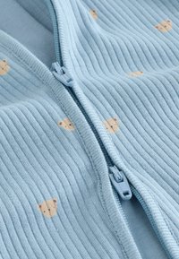 Tela acanalada azul claro con una cremallera doble y pequeños estampados en beige con cara de oso dispersos por todo el material.