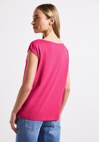 Top corto fucsia de manga corta con escote redondeado, textura suave y corte relajado, combinado con jeans de mezclilla azul claro.