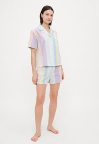 Korte mouwen pyjama-set in pastelkleurige strepen; de top heeft een zak, gestructureerde textuur en bijpassende shorts. Lichtgewicht katoenmateriaal.