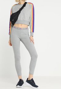 Szara, krótka bluza z wielokolorowymi paskami, szare legginsy, czarna torba na ramię i granatowe trampki; casualowy, sportowy zestaw.