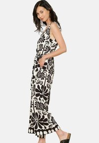 Črno-bela cvetlična kombinezona z pasom, širokimi hlačnicami in okroglo izrezom. Ima velik cvetlični vzorec in stranske žepke.