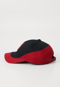 Baseball cap with a black crown and red brim. Features an adjustable strap at the back and a logo detail on the front. Cotton material.