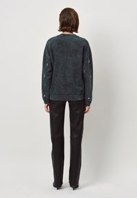 Donkergrijze, oversized sweatshirt met een vervaagd textuur en geribbelde manchetten. Draagt in combinatie met strakke zwarte leren broek en hakken. Achteraanzicht.