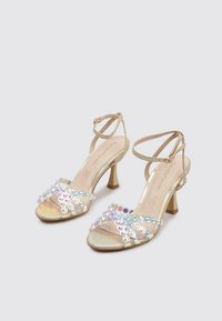 Sandalias de tacón alto con tiras, que presentan una base de color beige claro, detalles iridiscentes a lo largo de las tiras y un tacón cuadrado de 5 cm.