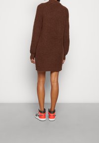 Brun stickad klänning med hög krage, långa ärmar och avslappnad passform, nedstoppad med högskaftade sneakers med orange detaljer.