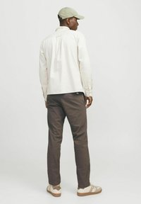 Helle Langarmbluse, dunkle Hose und beige Sneakers mit braunen Akzenten; Cap mit flacher Krempe. Einfaches, funktionales Design.