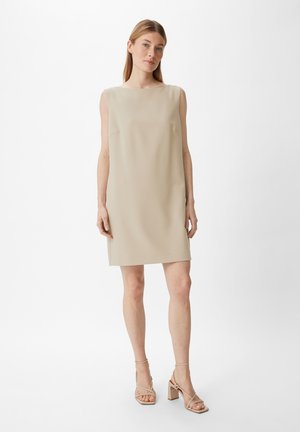 Robe tunique sans manches beige avec une silhouette droite, un minimum de détails et une texture lisse. Associée à des sandales à talons beiges.