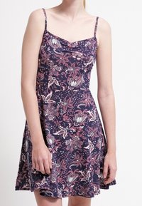 Blommig skaterklänning i marinblå med tunna band, en figurnära överdel och en utsvängd kjol; tyget har en mjuk textur.